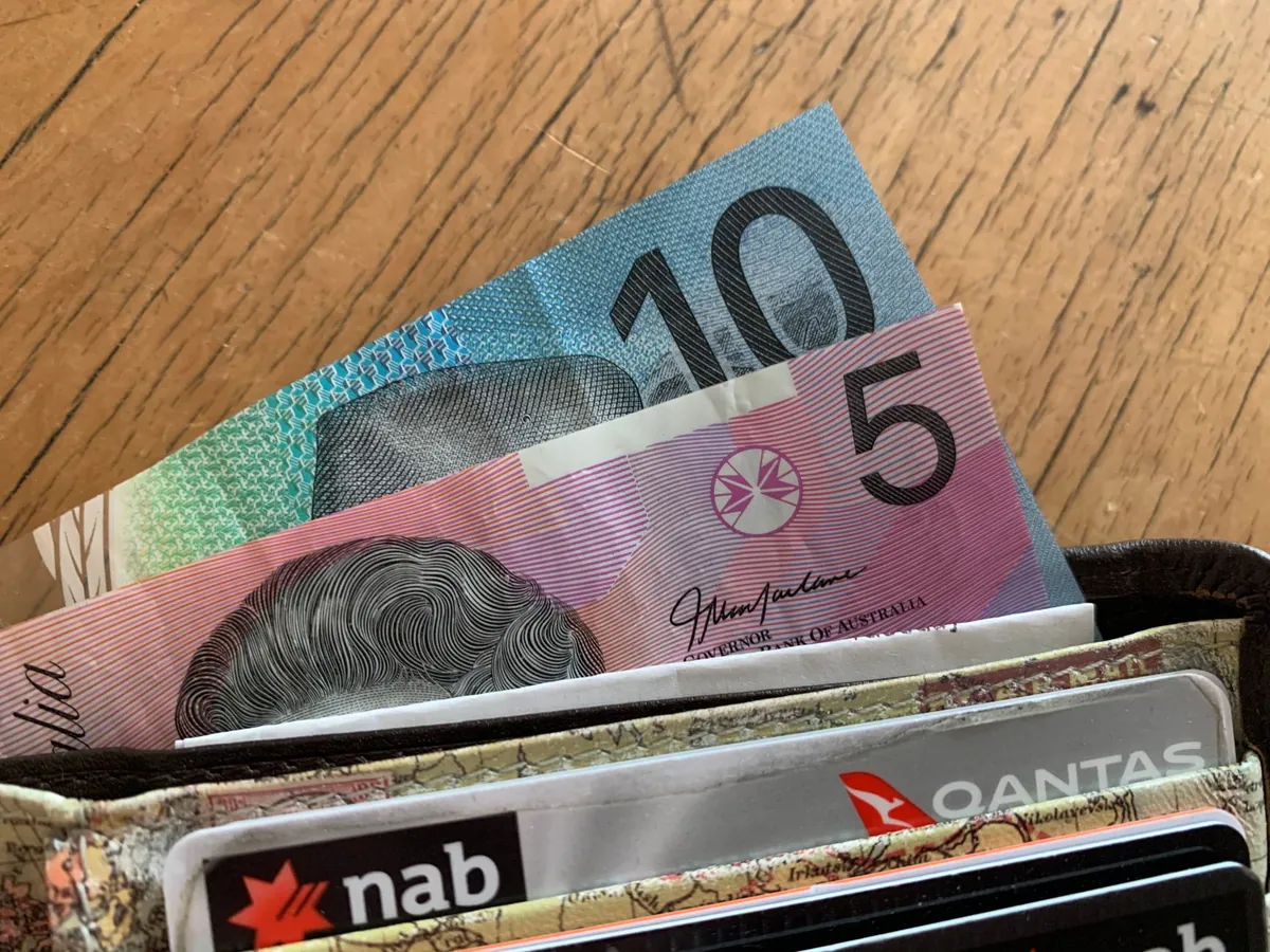 Close-up of Australian dollar bills and credit cards in a wallet resting on a wooden surface.