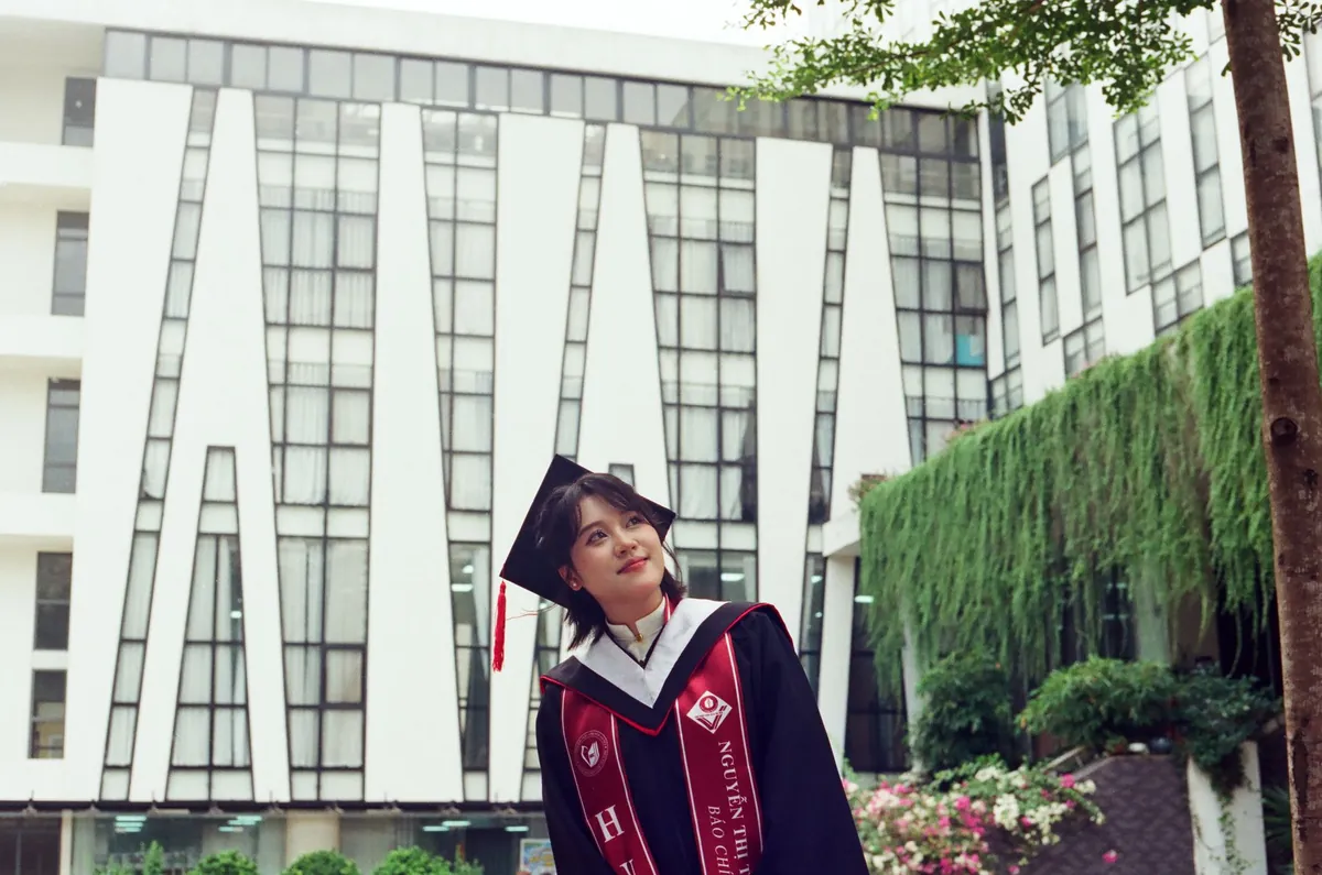 Joven graduada sonriendo al aire libre junto a arquitectura moderna, con toga y birrete.